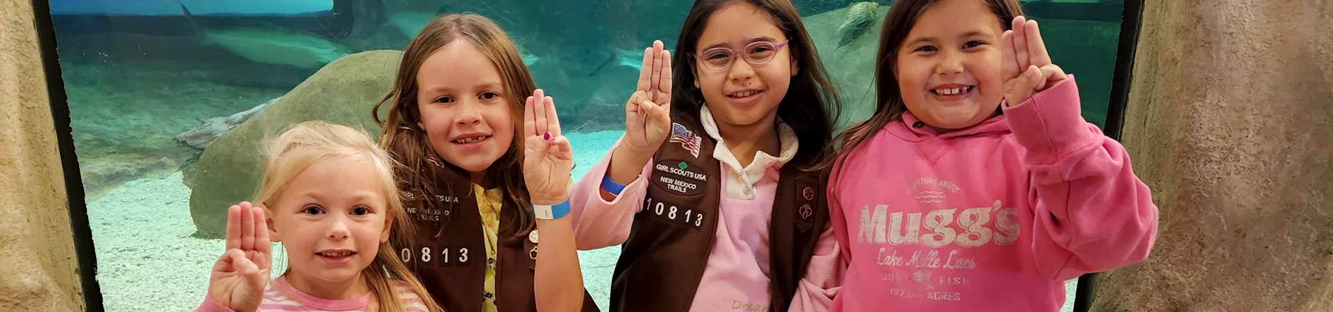  two girl scouts wearing trefoil clothing leaning on one another indoors 